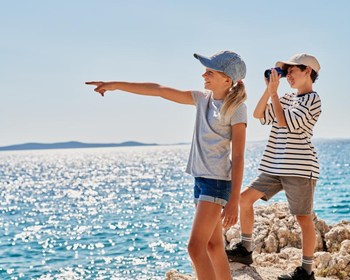 Two teenagers are playing outdoors, standing on the cliff edge and looking into the distance.